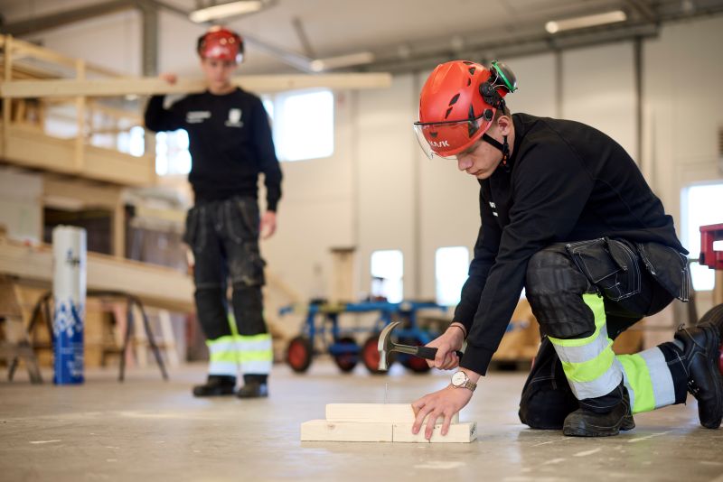 Två elever som bär på virke att bygga med. 